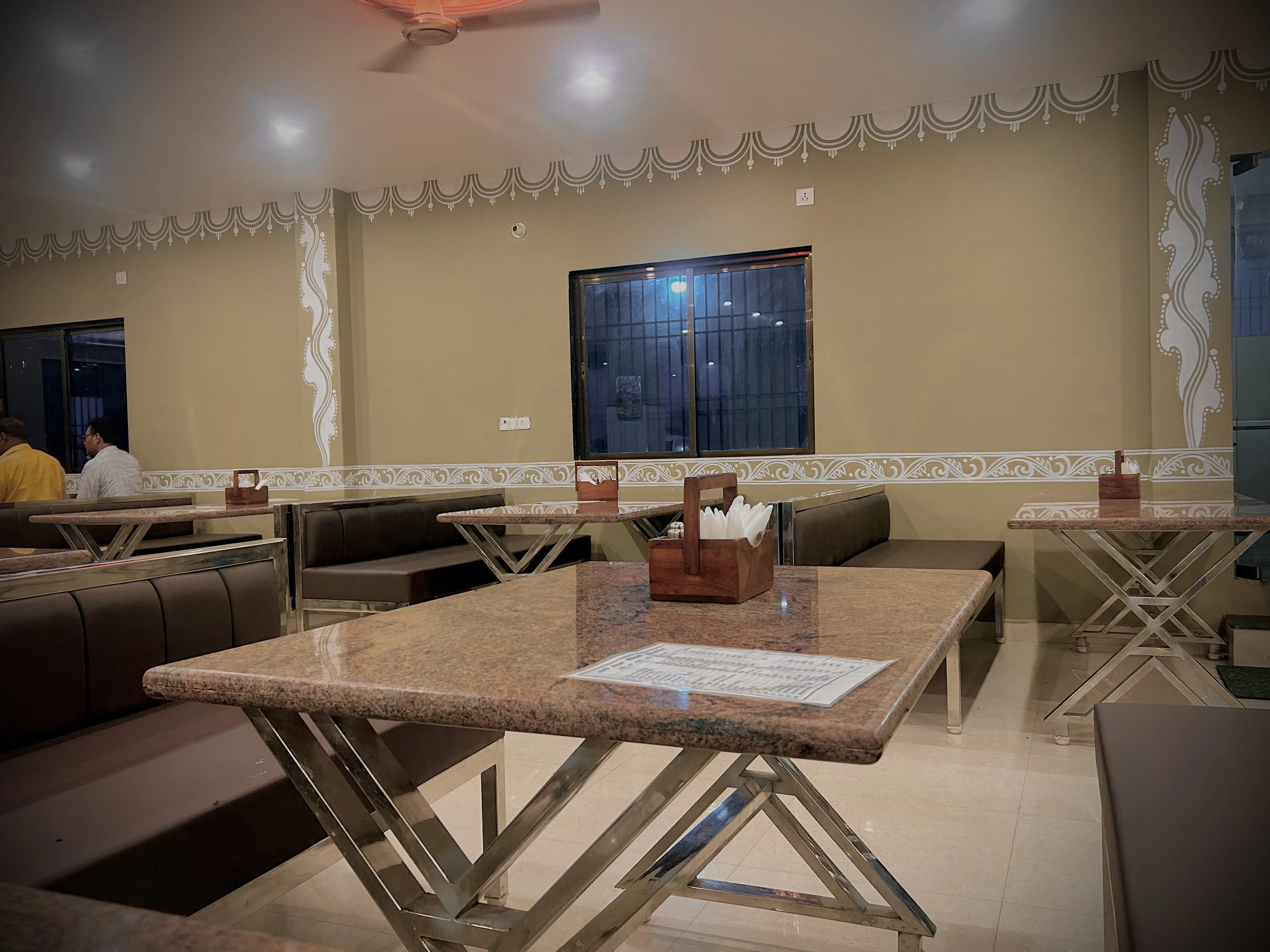 Dining room with carved sandstone arches, maroon seating and brass lanterns